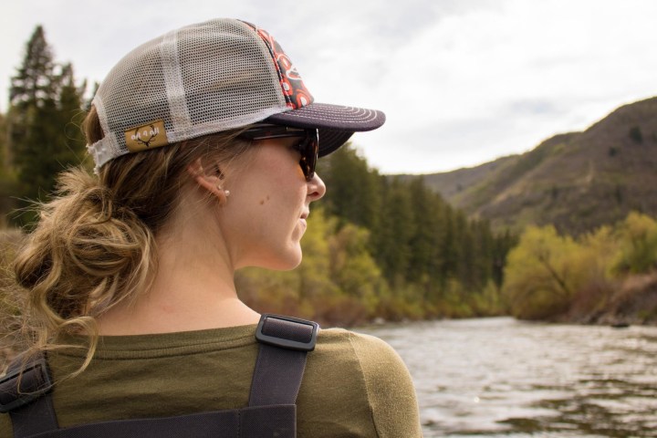 a man wearing a hat and sunglasses in front of a body of water
